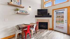 A dining area with a wooden table, red and white chairs, a fireplace, and a TV mounted above it. - Lrd204d2 (Dillon)