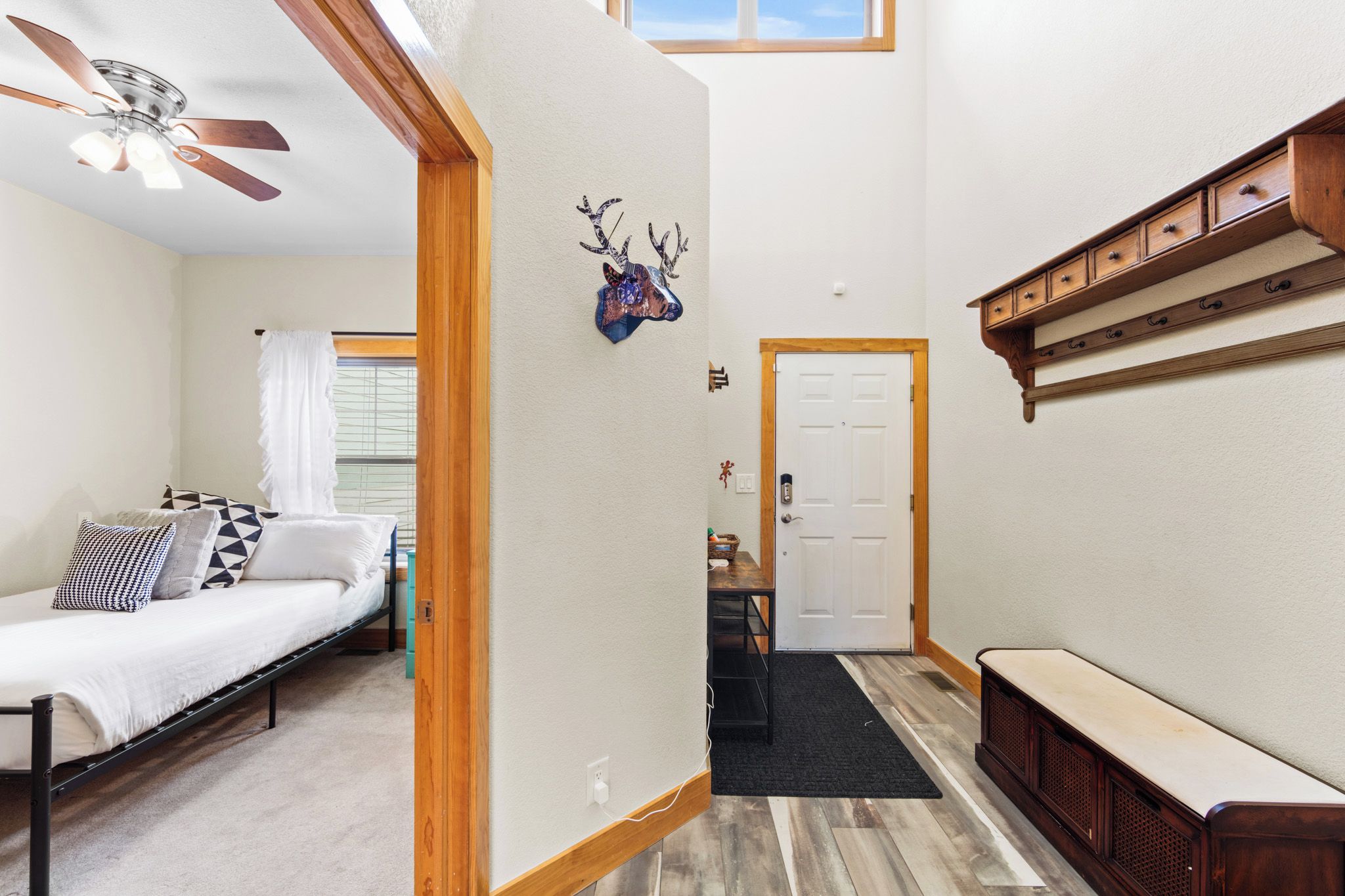 Une chambre à coucher avec un lit, un ventilateur de plafond, une fenêtre avec des rideaux et un banc en bois.