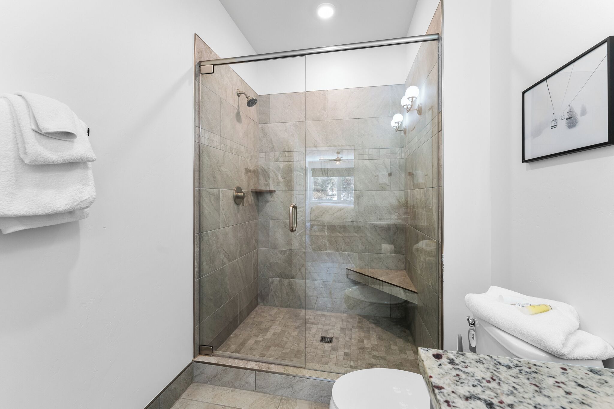A modern bathroom with a glass-enclosed shower, a white toilet, and a marble sink.