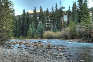 A river with rocks and trees, a building with multiple stories in the background. - Clearwater Lofts #203, Building 2 (Keystone)