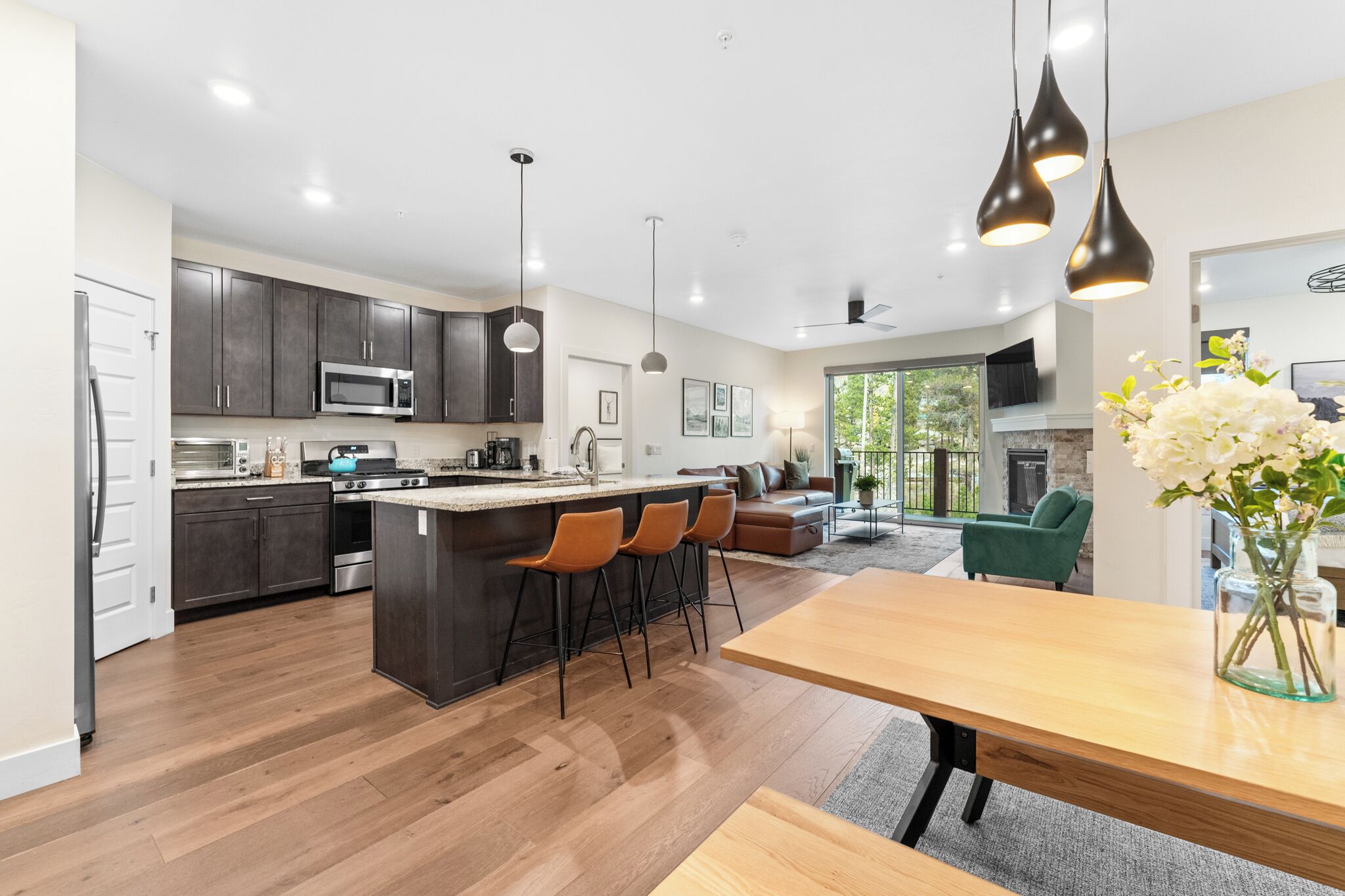 A modern kitchen with dark cabinets, a central island with bar stools, and pendant lighting. - Clearwater Lofts #203, Building 2 (Keystone)