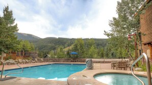 Una piscina con hidromasaje, sillas de descanso y vistas a una cadena montañosa boscosa.