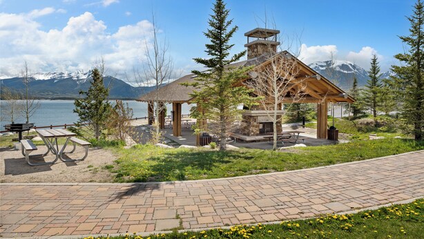 A lodge with a stone chimney, picnic tables, and a view of a lake and mountains. - Lc307ad1 (Dillon)