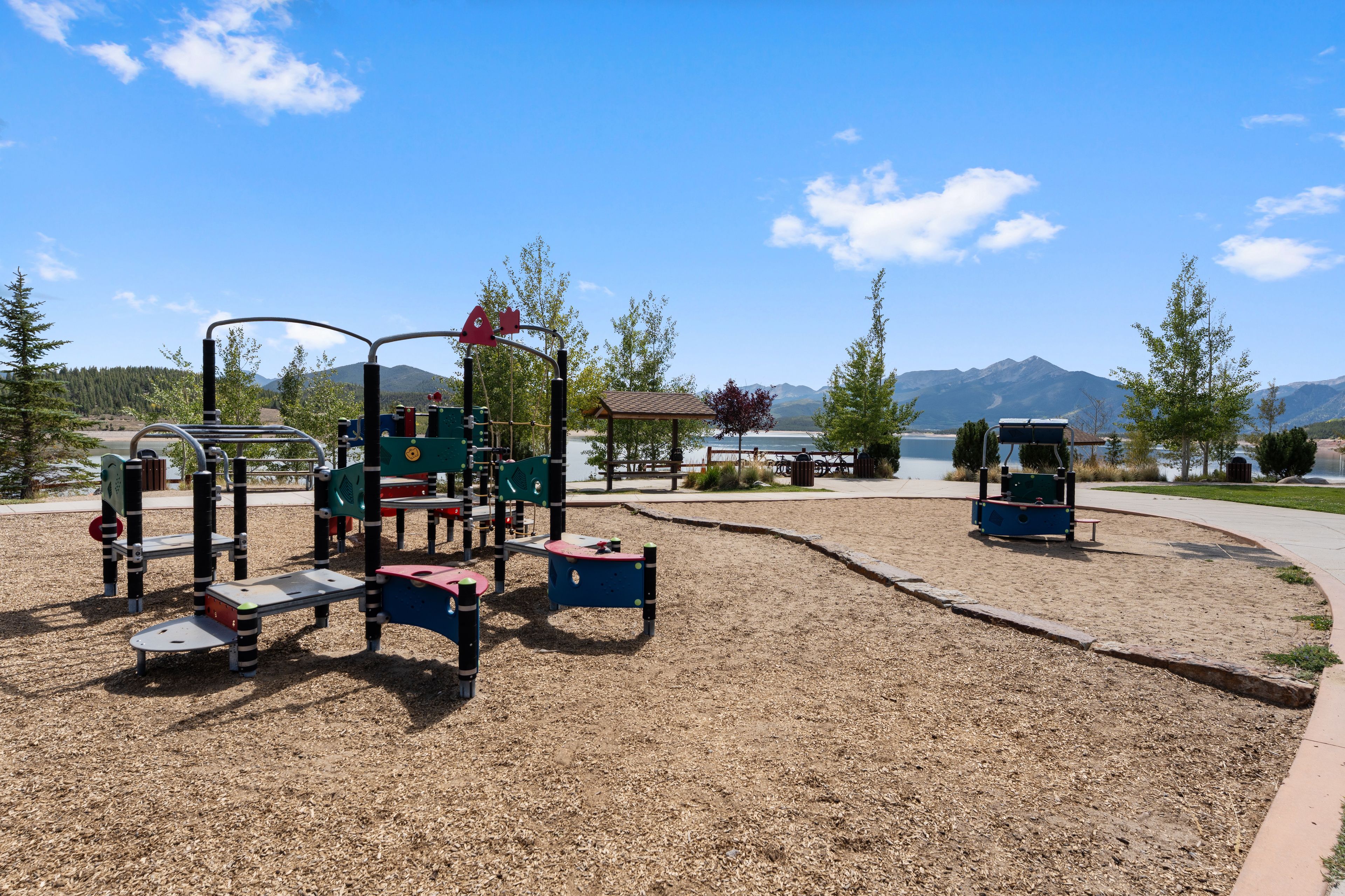 Un parque infantil con diversas estructuras de juego, un área de picnic y vistas a montañas al fondo.