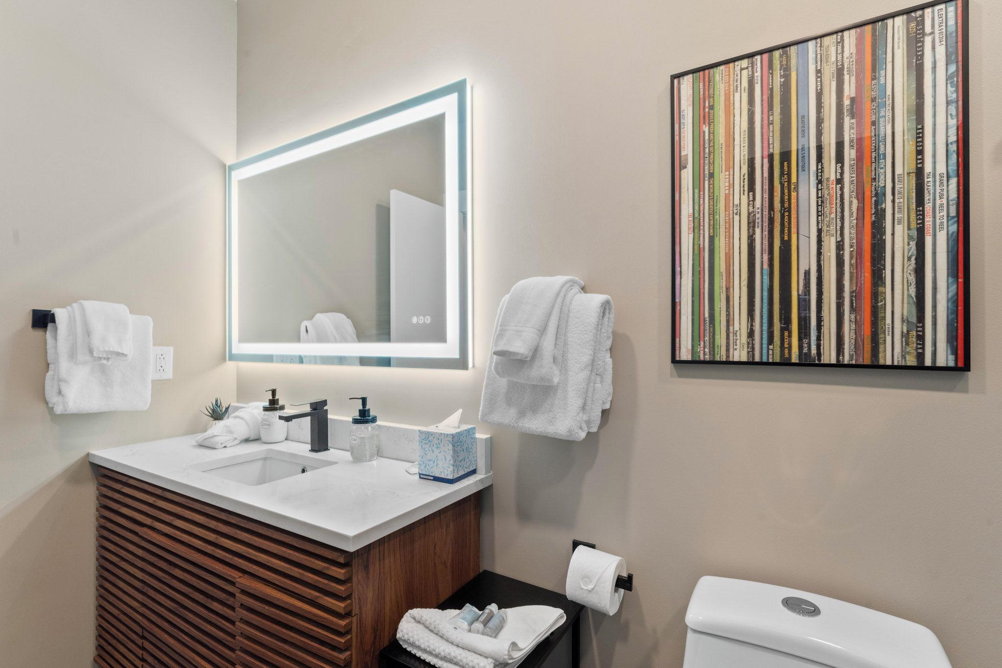 A modern bathroom with a large mirror, dual sinks, a wooden vanity, a toilet, and a wall-mounted towel rack.