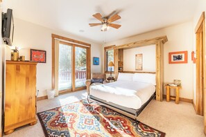 Un dormitorio con cama, ventilador de techo, cómoda de madera, alfombra y ventana con vistas.