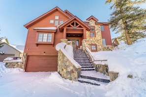 Una casa de dos pisos con una escalera de piedra que lleva a la puerta principal, rodeada de nieve.