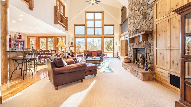 A spacious living room with a stone fireplace, wooden cabinets, and a large window overlooking a mountain. - 94rgrs4 (Silverthorne)