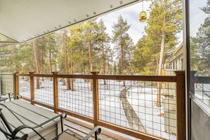 A balcony with a wooden railing, a bench, and a view of a snowy forest with tall trees.