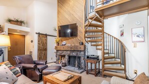 A living room with a fireplace, leather chairs, a wooden coffee table, a TV, and a spiral staircase.