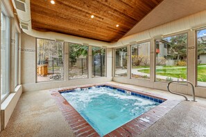 A hot tub with a wooden ceiling and large windows overlooking a backyard.