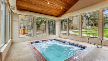 Un jacuzzi con techo de madera y amplias ventanas que dan a un jardín trasero.