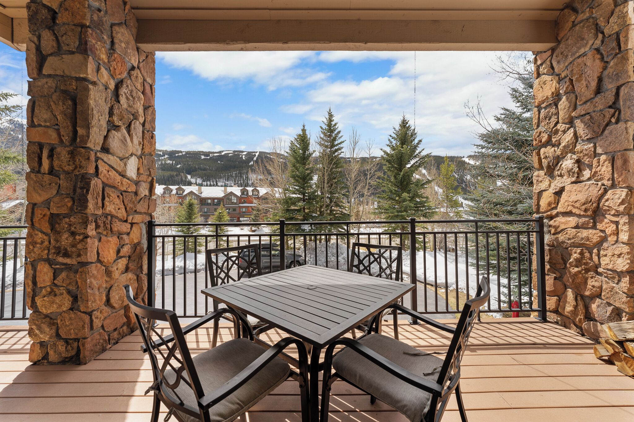 Eine Terrasse mit Steinsäulen und einer Sitzgruppe mit Tisch und Stühlen, mit Blick auf eine verschneite Landschaft und Gebäude.