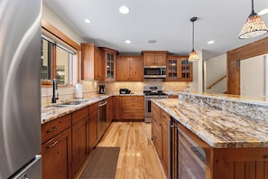 Una cocina moderna con gabinetes de madera, encimeras de granito, electrodomésticos de acero inoxidable e iluminación colgante.
