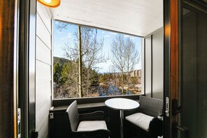 A room with a large window, a small round table, and two wicker chairs.