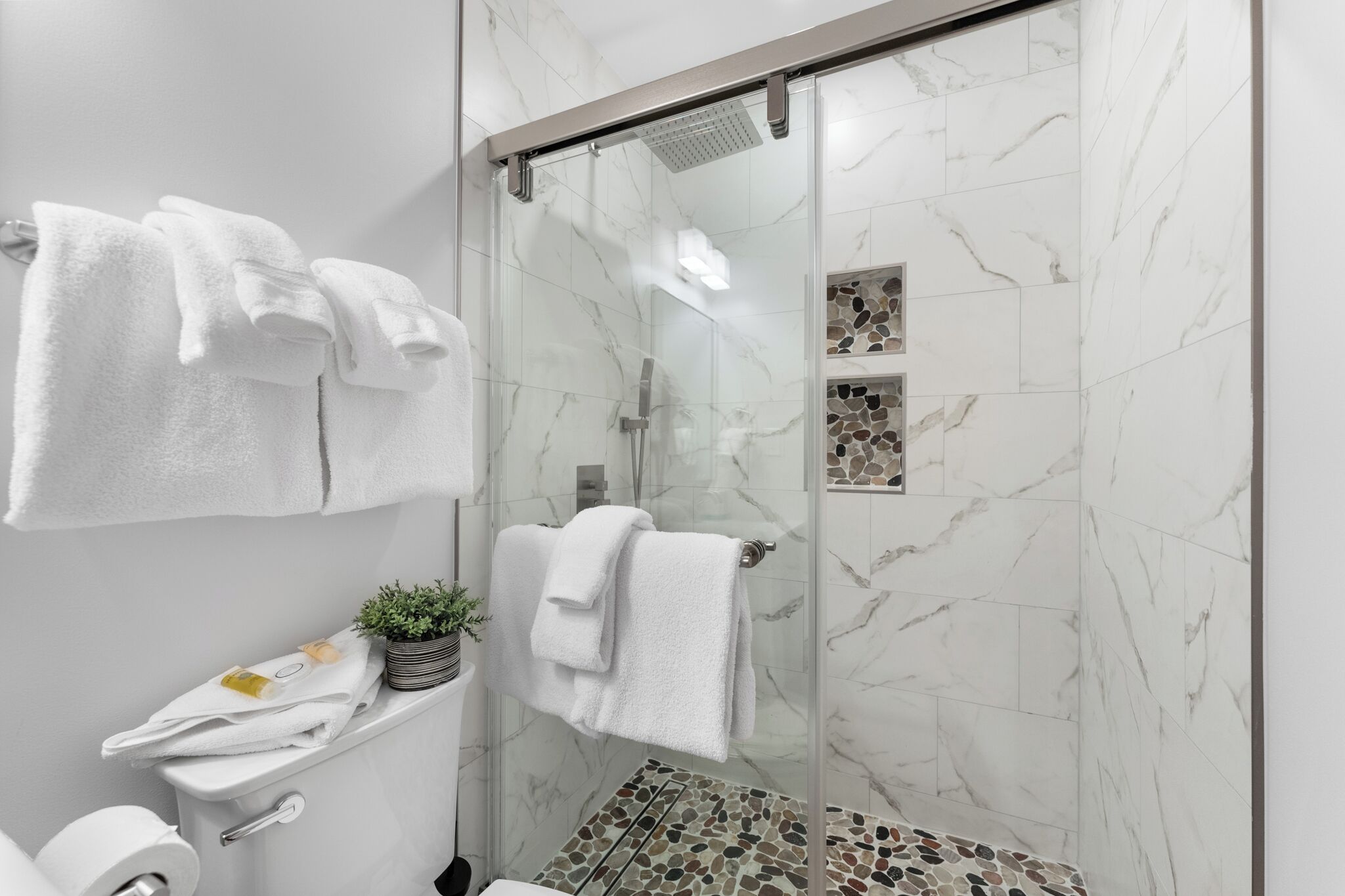 A modern bathroom with a glass shower enclosure, marble tiles, and neatly arranged towels.