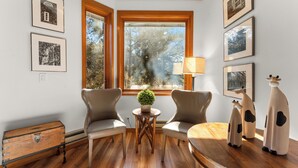 A room with two leather chairs, a wooden table, a small potted plant, and a lamp. There are framed pictures on the walls and a window with a view of trees. - Tt1327-3 (Keystone)