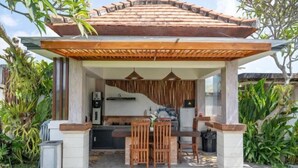 A covered outdoor seating area with a wooden table and chairs, surrounded by plants and a tiled floor. - Villa d'Alas Ubud (Bali)