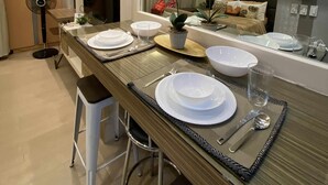 Un espace repas moderne avec une longue table dressée pour quatre personnes, un ventilateur et une plante en pot.