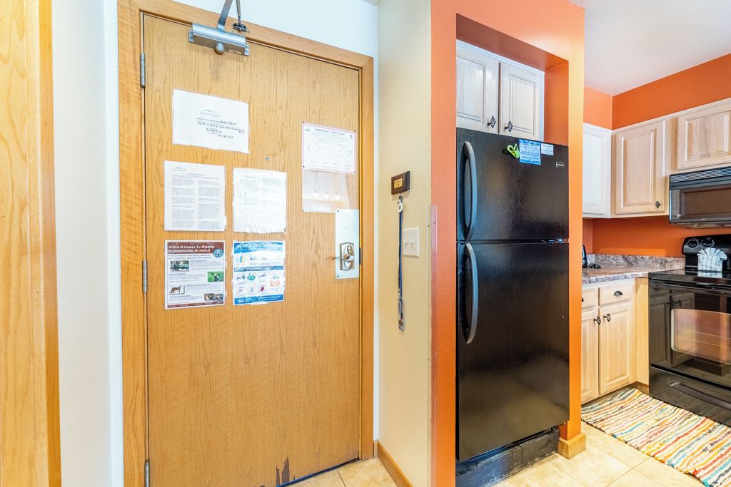 A kitchen with a black refrigerator, wooden cabinets, and a microwave.