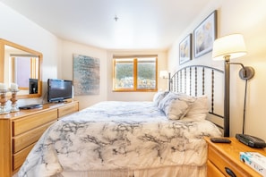 A hotel room with a bed, a television, a desk with a lamp, and artwork on the walls.