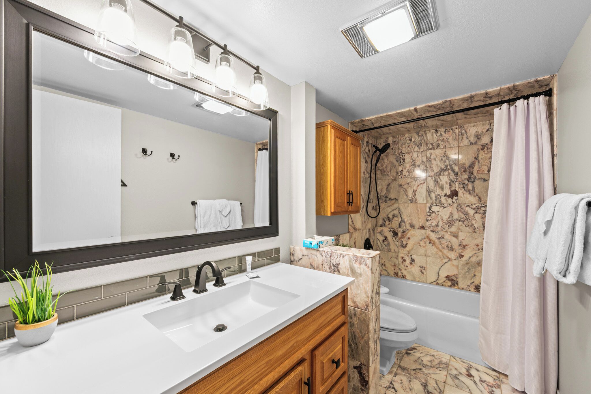 A modern bathroom with a large mirror, a sink, a shower, and a toilet.