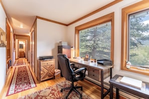 A home office with a desk, chair, and large window with a view of trees.