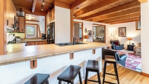 A spacious kitchen with wooden beams, a large island with bar stools, and a view into the living area. - Tt1340-3 (Keystone)