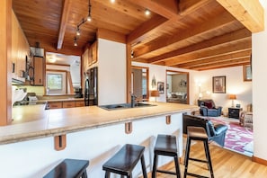 A spacious kitchen with a wooden ceiling and bar stools.
