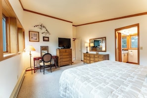 A bedroom with a bed, desk, chair, dresser, television, and a mirror.