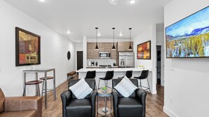 Un salon moderne avec une cuisine en arrière-plan, comprenant un coin repas avec des chaises noires et une table basse.
