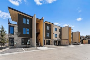 Un edificio moderno de varios pisos con fachadas de madera y piedra, varios portones de garaje y un cielo despejado.