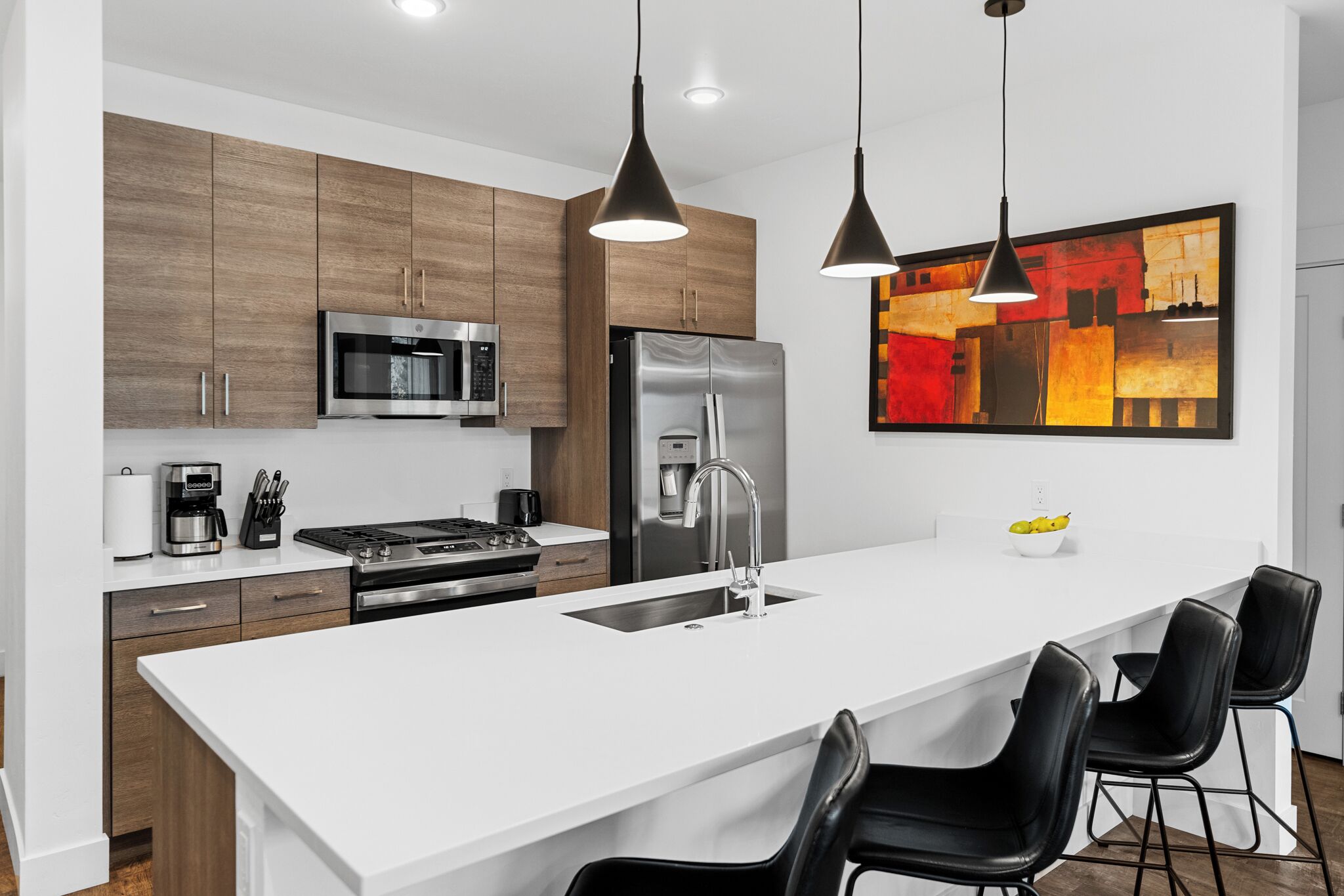 Cozinha moderna com uma ilha grande, eletrodomésticos de aço inoxidável e luminárias pendentes pretas.