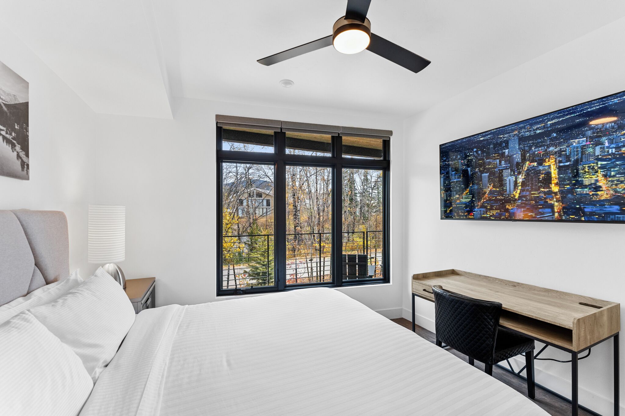 Un dormitorio moderno con una cama grande, un escritorio y un cuadro de un paisaje urbano.