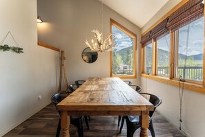 A dining area with a wooden table, black chairs, a chandelier, and large windows with a view of mountains.