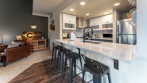 A modern kitchen with a marble countertop, stainless steel appliances, and a bar area with stools. - Qs1606-2 (Keystone)