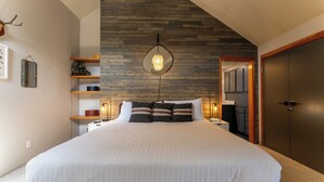 A modern bedroom with a large bed, wooden wall paneling, a hanging light fixture, and a wooden door. - Qs1606-2 (Keystone)