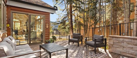 A covered patio with outdoor furniture, a stone wall, and a view of trees and a building.