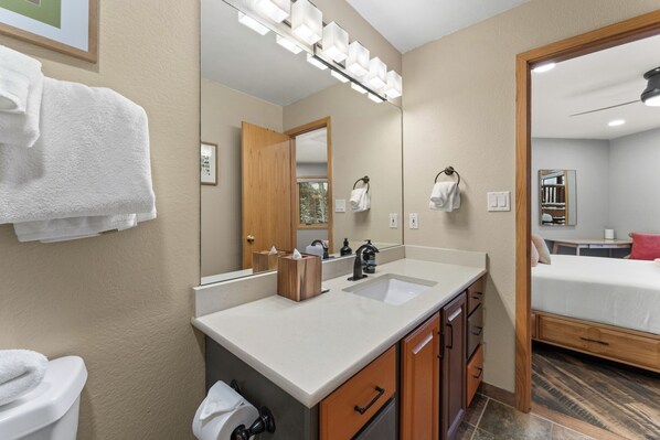 A hotel bathroom with a double sink, wooden cabinets, a mirror, and a bed in the adjacent room. - 341bhcs3 (Silverthorne)