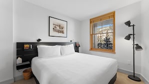 A neatly arranged bedroom with a large bed, a framed picture on the wall, a window with a view of trees, and a floor lamp. - Silver Mill #8220 (Keystone)