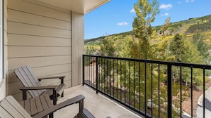 A balcony with two Adirondack chairs and a small table, overlooking a scenic view of a forested hillside. - Silver Mill #8220 (Keystone)