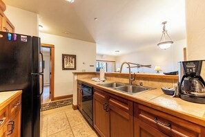 A kitchen with wooden cabinets, a black refrigerator, a double sink, and a coffee maker. - Og203-1 (Keystone)