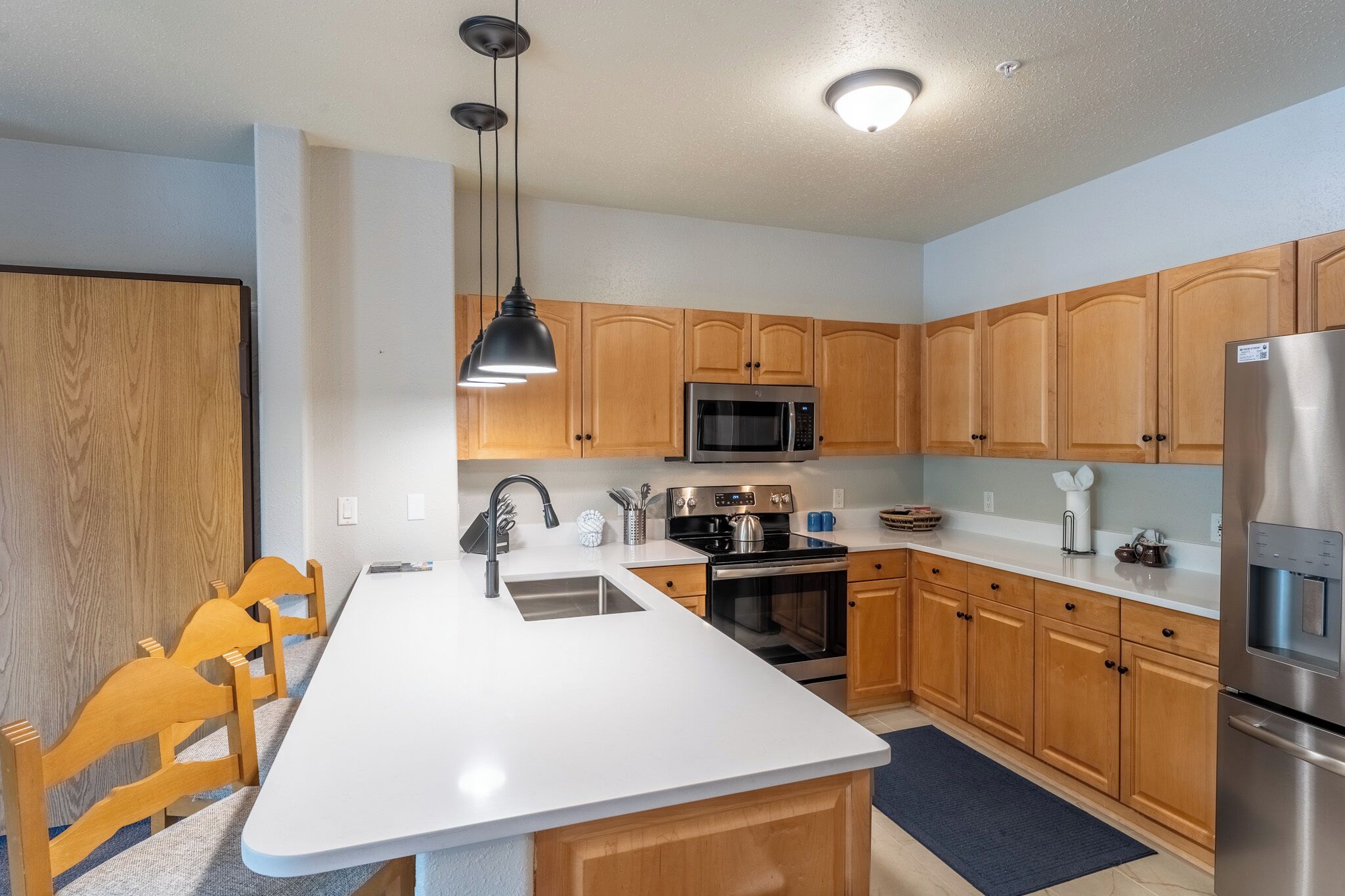 A modern kitchen with wooden cabinets, a stainless steel refrigerator, a microwave, and a stove.