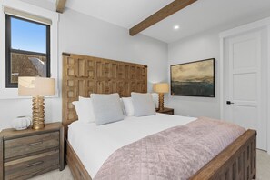 Ein Schlafzimmer mit einem hölzernen Kopfteil, einem großen Bett mit gesteppter Bettdecke, Nachttischlampen, einem Nachttisch und einem gerahmten Bild an der Wand.