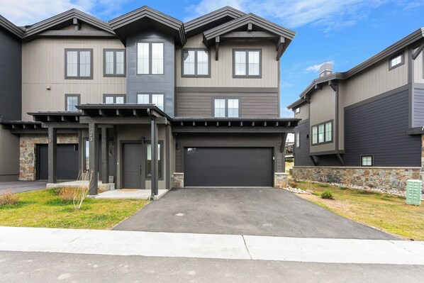 A modern two-story residential building with a garage, stone accents, and a well-maintained driveway.