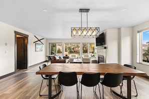 A spacious dining area with a large wooden table and black chairs, a modern chandelier, and large windows offering a view of the outdoors. - 23fhs4 (Silverthorne)