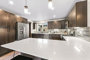 A modern kitchen with dark wood cabinets, stainless steel appliances, and a large white marble countertop.