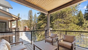Eine überdachte Terrasse mit Holzmöbeln und einem Kamin aus Stein, mit Blick auf einen bewaldeten Bereich.