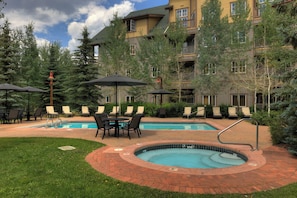 A pool area with lounge chairs, a hot tub, and a building with balconies. - Expedition Station #8573 (Keystone)