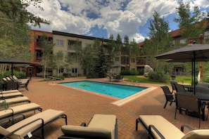 A pool area with lounge chairs and umbrellas, surrounded by trees and buildings. - Expedition Station #8573 (Keystone)